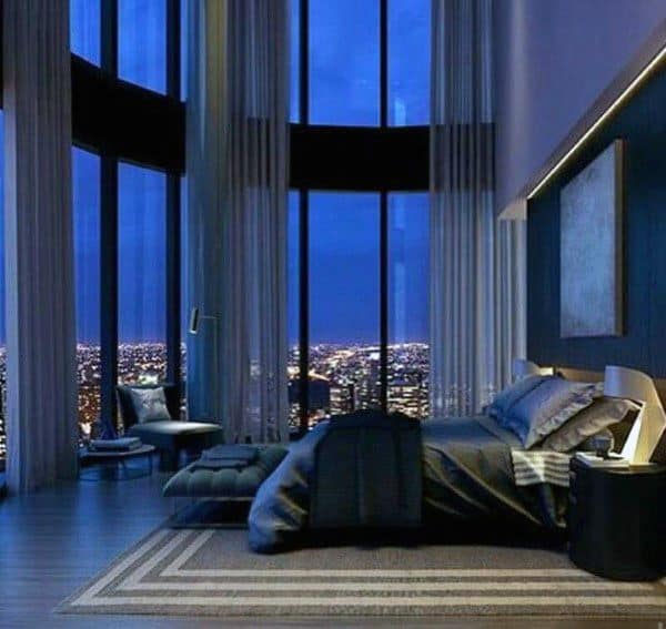 Luxury bedroom with tall glass windows, city skyline view, and dark modern decor.