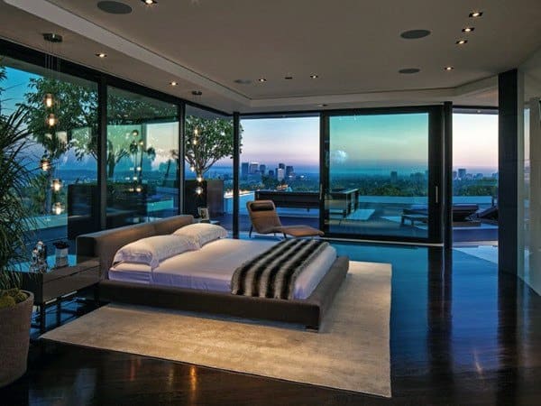 Modern bedroom with city view, glass walls, and sleek contemporary furnishings.