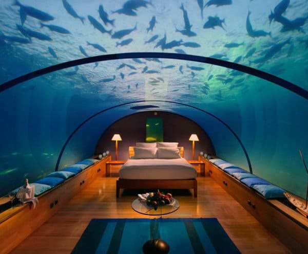 Underwater bedroom with glass ceiling, ocean view, and marine life above.