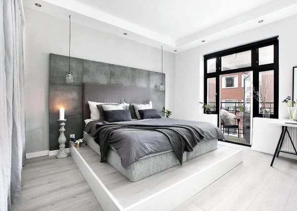 Minimalist bedroom with gray bedding, elevated platform, and natural light.