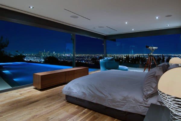 Luxury bedroom with glass walls, city skyline view, and infinity pool at night.