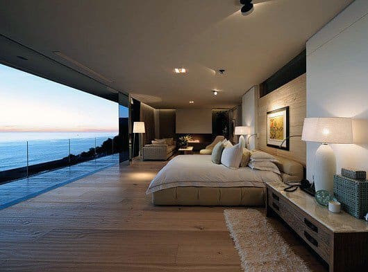 Spacious bedroom with ocean view, glass walls, and cozy wooden interior design.