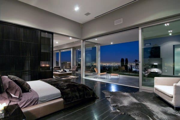 Modern bedroom with glass walls, city view, and sleek black furnishings.