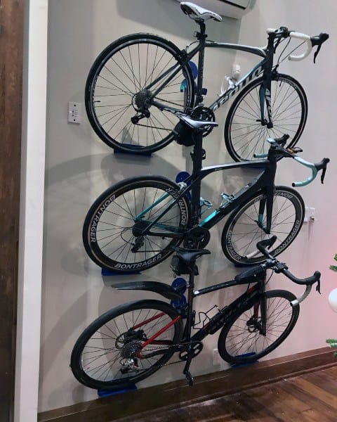Vertical wall-mounted bike rack holding three bicycles in an organized indoor space.
