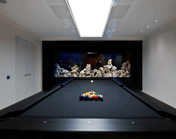 A modern billiards table in a sleek, minimalist game room with a wall-mounted aquarium.