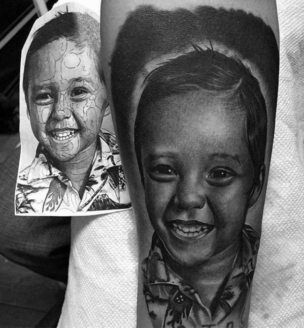 Black and white tattoo of a smiling child next to the original sketch on paper