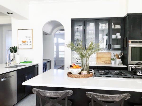 Black kitchen cabinets with glass doors, white countertops, and a central island decor.
