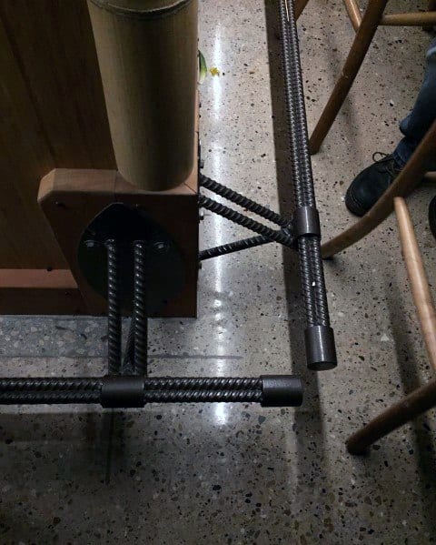 Industrial-style black rebar foot rail attached to a wooden bar on polished concrete floor.