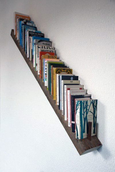 Wall-mounted diagonal bookshelf holding books of various colors against a white wall