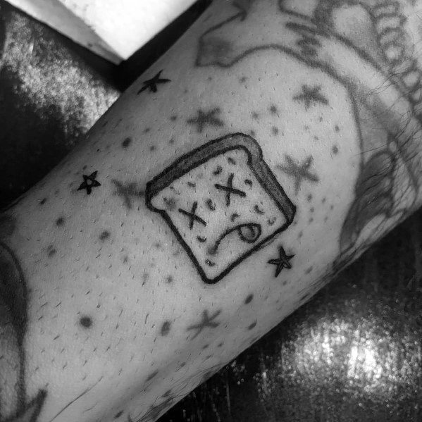 Minimalist black ink tattoo of a cartoon-style toast with X eyes and a tongue out, surrounded by small stars for a playful and edgy look.