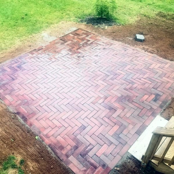 Brick patio in a herringbone design, beautifully encircled by lush green grass