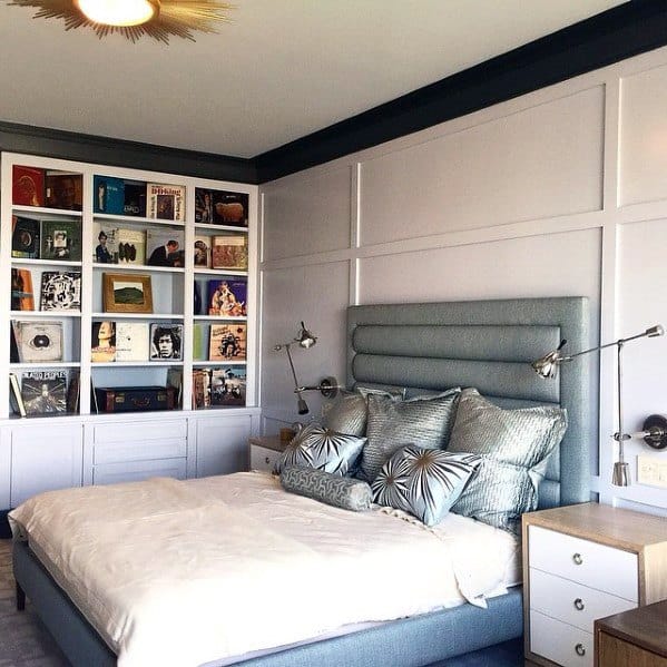 Bedroom with built-in bookcase featuring colorful albums, a gray upholstered headboard, and stylish lighting