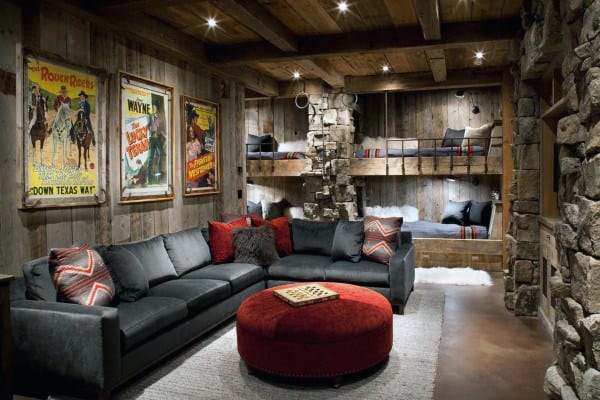 Cozy rustic room with bunk beds, vintage posters, a gray couch, red accents, and stone bunk-lined walls