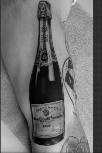 Tattoo of a detailed champagne bottle on an arm, featuring the label of a well-known brand.