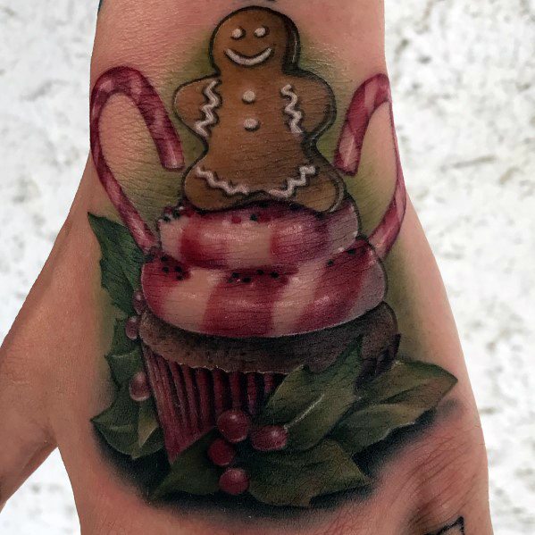 Festive Christmas tattoo featuring a gingerbread man on a candy cane-topped cupcake with holly leaves and berries for a holiday touch.