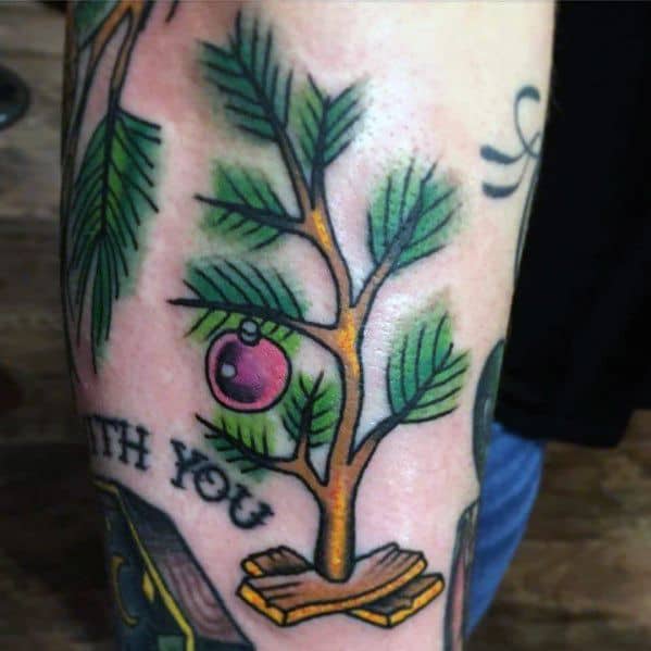 Charlie Brown-inspired Christmas tree tattoo with sparse branches, a single red ornament, and a wooden base, capturing a nostalgic holiday feel.