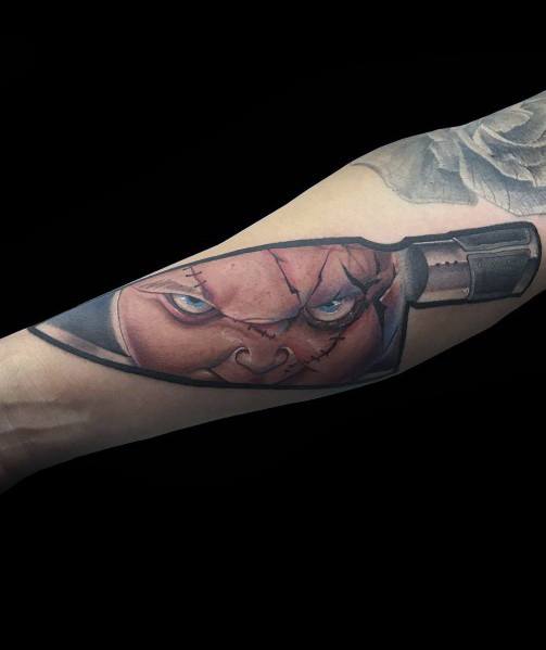 Chucky tattoo with his intense gaze reflected in a realistic knife blade, creating a chilling and creative horror-inspired design.