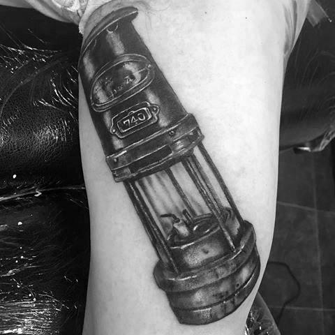 Realistic black and grey tattoo of a vintage miner's lamp with detailed shading on a person's arm.