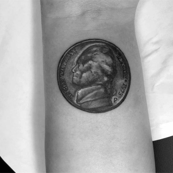 Realistic tattoo of a 1973 Jefferson nickel on the wrist, featuring detailed shading and depth for a lifelike coin design