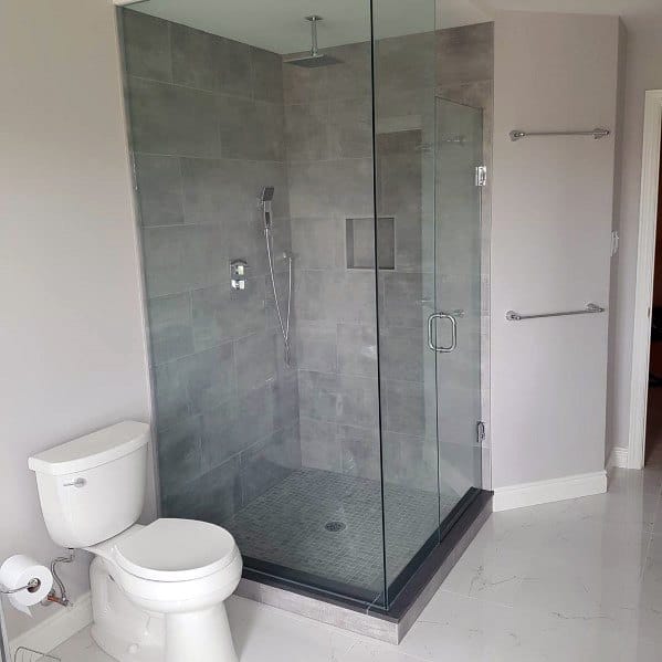 Modern bathroom with a corner glass-enclosed shower, gray tiles, toilet, and white walls