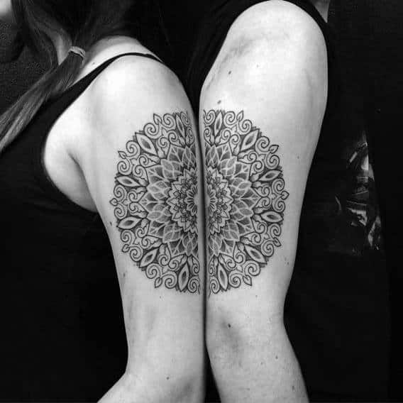 Matching mandala tattoos on upper arms that form a complete circular design when the couple stands back to back.