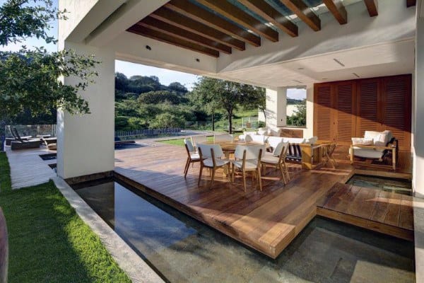 Covered wooden deck with outdoor dining area, water features, and a view of lush greenery.