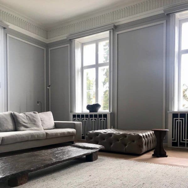 A stylish living room with elegant crown molding, a minimalist sofa, tufted ottoman, and large windows