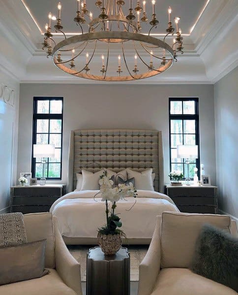 Elegant master bedroom with crown molding lighting, tufted headboard, and cozy seating
