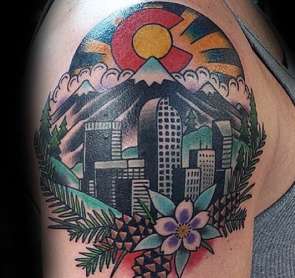 Colorful Denver skyline tattoo with mountains, Colorado flag sun, pinecones, and a columbine flower on the upper arm.