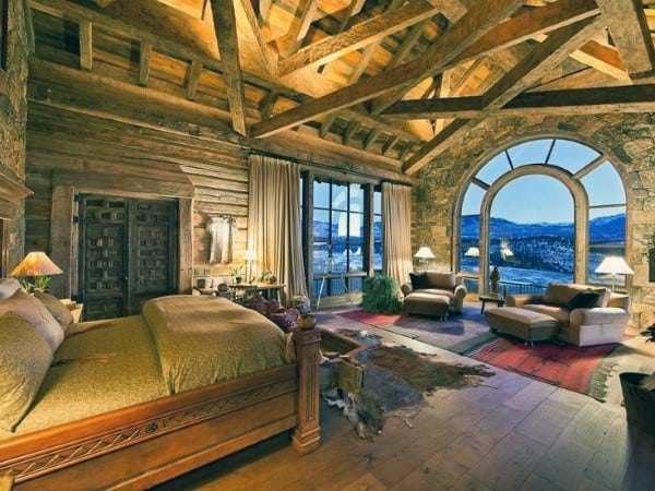 Rustic bedroom with vaulted ceiling, arched window, and stunning mountain view.