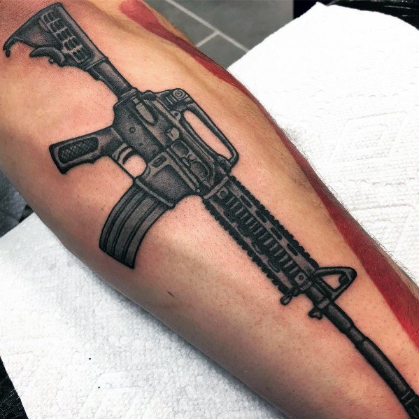 Black and grey AR-15 tattoo on the leg, featuring bold shading and intricate details, symbolizing strength, precision, and tactical readiness.