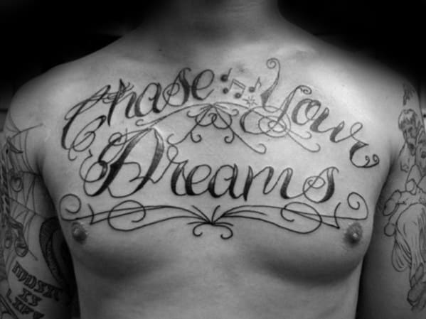 Chest tattoo with ornate script that reads "Chase Your Dreams," surrounded by decorative swirls and flourishes.