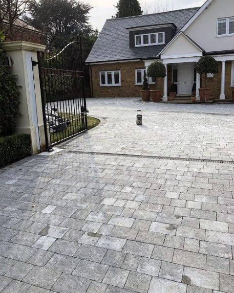 Paved driveway with gray stone tiles leading to a gated entrance and a traditional-style home.