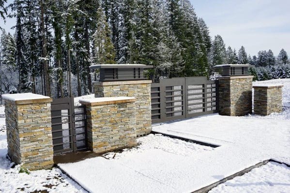 Modern driveway gate with horizontal metal slats and stacked stone pillars.