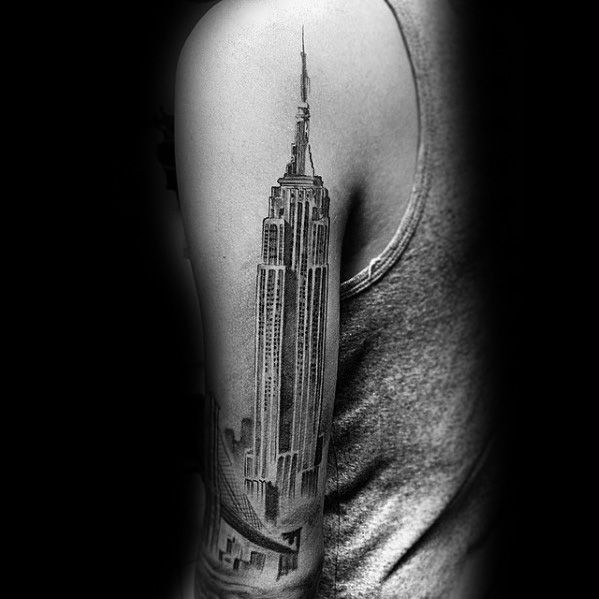 Empire State Building tattoo in detailed black shading, vertically placed along a man's upper arm.