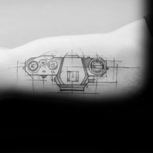 Tattoo of a game controller drawn in a technical blueprint style with sketch lines, positioned along the inner arm for a sleek modern look.
