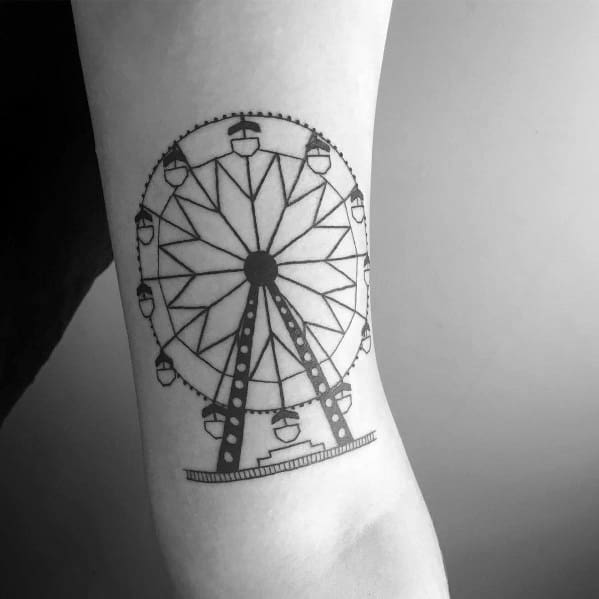 Minimalist black ink Ferris wheel tattoo with geometric spokes and small gondolas, placed on the inner forearm for a clean look.