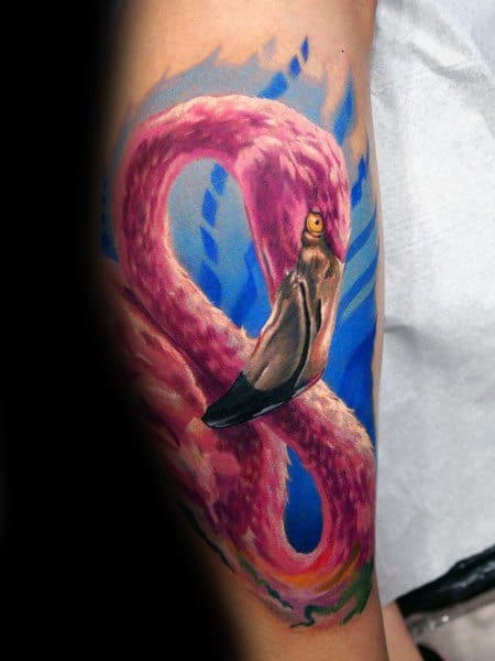 Realistic flamingo tattoo on upper arm with vivid pink feathers, detailed shading, and a dynamic blue background for contrast.