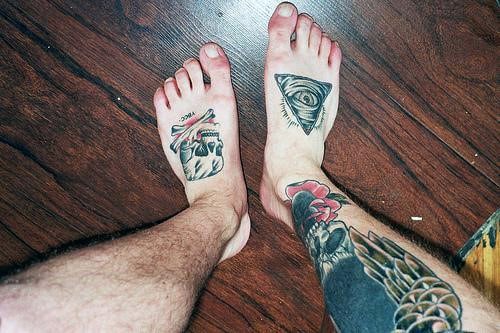 Bare feet with skull design on one foot and an eye within a triangle on the other