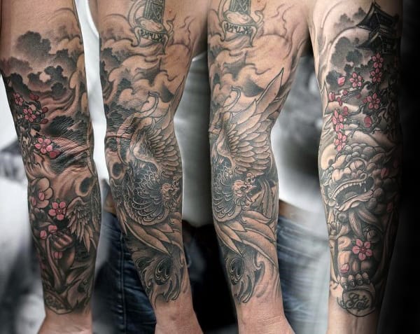 Intricate forearm tattoo featuring a phoenix, cherry blossoms, swirling clouds, and a fierce dragon in a detailed black and grey design