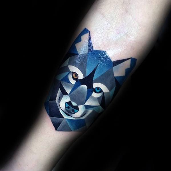 Cubist tattoo of a wolf's face in blue and grey tones, featuring sharp geometric shapes and heterochromatic eyes.