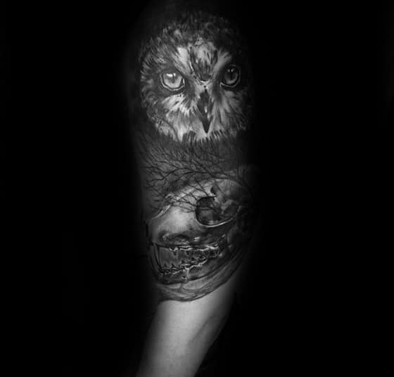 Realistic black and grey tattoo of an owl above a fox skull, set against leafless trees for a haunting forest vibe.