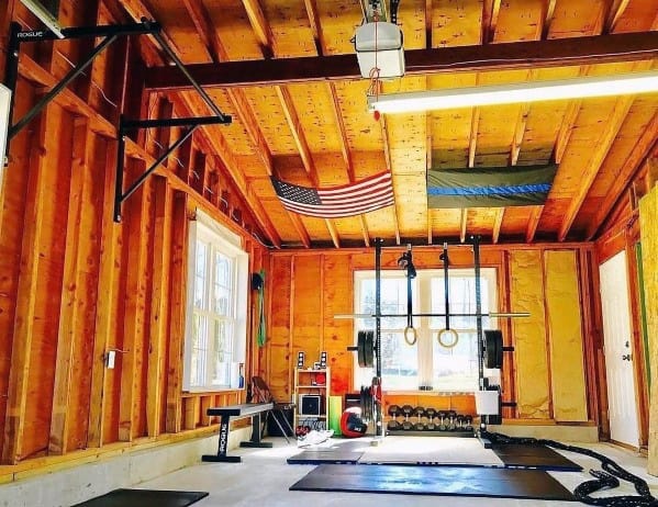 A rustic garage gym with pull-up bar, rings, weights, dumbbells, and organized fitness tools.
