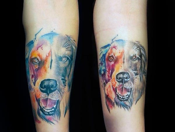 Watercolor-style Golden Retriever tattoo on forearms, blending vibrant blues, reds, and oranges with a detailed, expressive dog portrait.