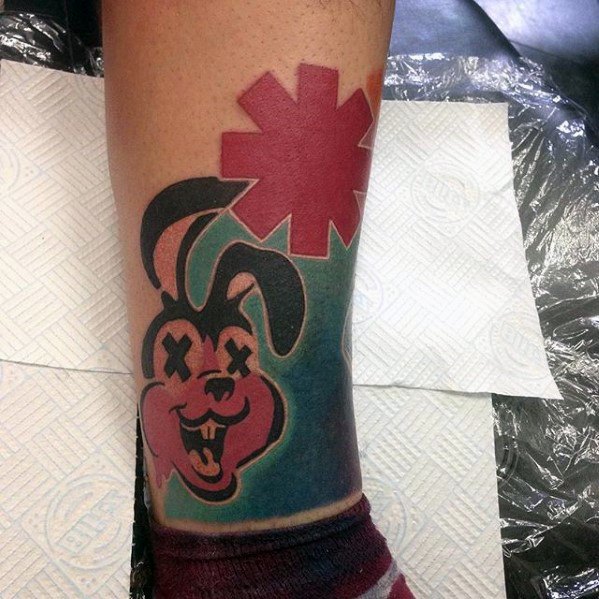Tattoo of a grinning X-eyed bunny with a bold red asterisk above it, set against a blue and green background on the leg.