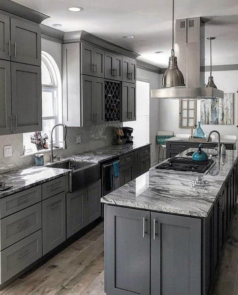 Dark grey kitchen with marble countertops, pendant lighting, and stainless steel farmhouse sink.