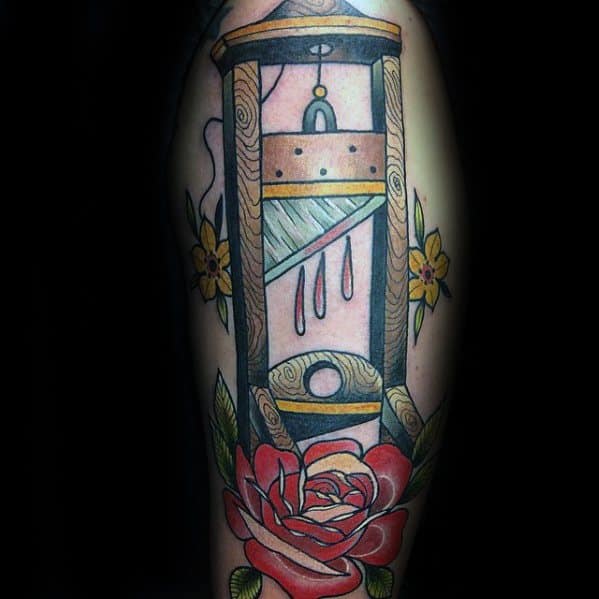 Traditional-style guillotine tattoo with dripping blood, surrounded by yellow flowers and a large red rose at the bottom.