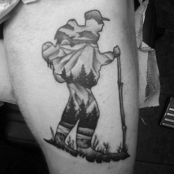 A black and gray tattoo of a hiker with a scenic mountain and forest landscape integrated into their silhouette, symbolizing a love for nature.