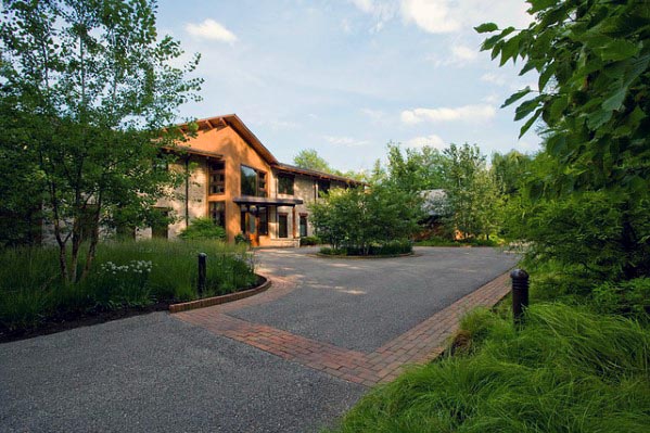 Paved driveway with brick accents surrounded by lush greenery leading to a modern house.