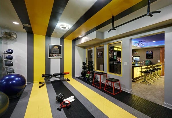 Colorful home gym with yellow and black striped walls, exercise equipment, and a bar area.